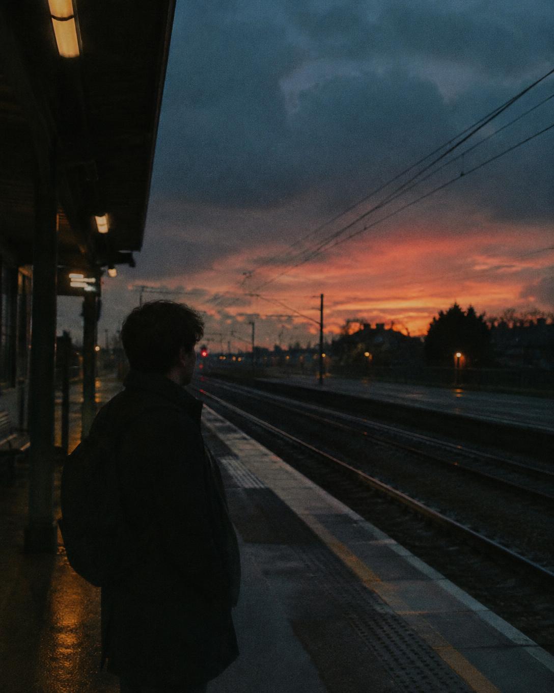 Vertical film still of a person waiting on a train platform at dusk